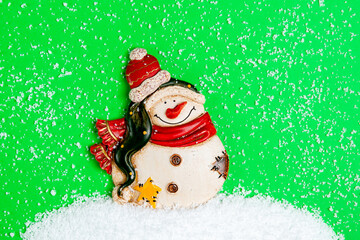 Snowman figurine on a green background. A snowdrift made of artificial snow. Christmas card.