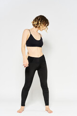 sporty woman in black jeans and a t-shirt doing exercises in a bright room