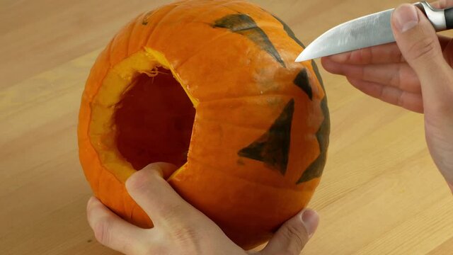 A man carves out a festive Halloween decor with his own hands. Scary pumpkin for Halloween in preparation. Drawing and carving pumpkin close-up.