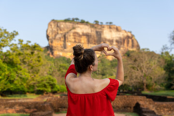 caucasian girl makes symbol of heart with her hand in fron of lion rock