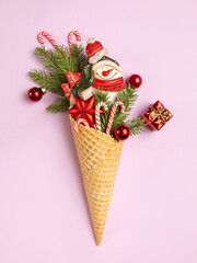Snowman, Christmas tree twigs and lollipop in a waffle cone. Christmas card. An original sweet gift. Pink background.