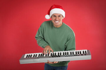 Man in Santa hat playing synthesizer on red background. Christmas music
