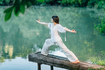 Fototapeta na wymiar Yoga by the Lake – Young woman practicing Warrior 2 Pose