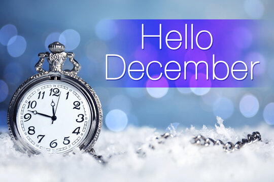 Greeting card with text Hello December. Pocket watch on snow against blurred Christmas lights