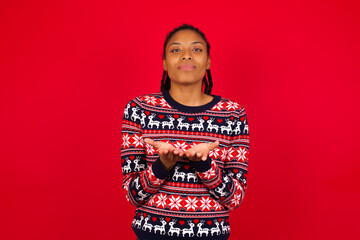 Young beautiful African American woman standing against red background holding something with open palms, offering to the camera.