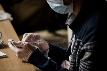 a man in a mask and gloves works through a mobile phone in a dark office at a table
