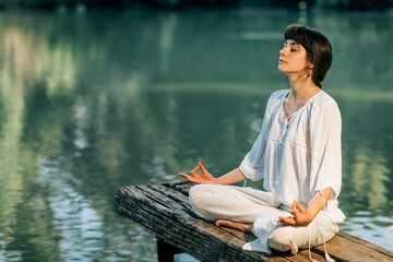 Yoga Retreat. Peaceful Young Woman Sitting in Lotus Position and Meditating by the Lake