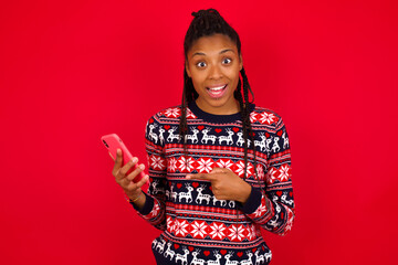 Young beautiful African American woman standing against red background holding in hands showing new cell,