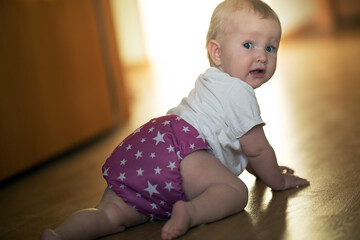 Baby girl wearing reusable diapers. Girl is crawling on the floor in the sun light