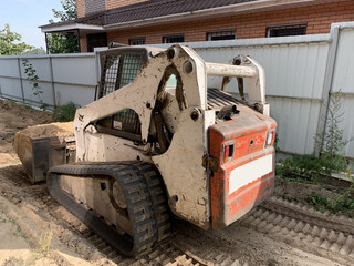 Small tractor with wide bucket. Small construction equipment. The crawler excavator levels the...
