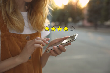 Woman leaving review online via smartphone outdoors, closeup. Four out of five stars over gadget
