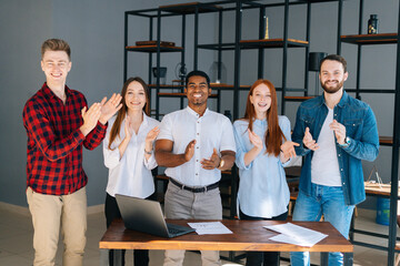 Cheerful group of multi-ethnic business people applauding and smiling gratefully looking into camera. Happy professional multiethnic business colleagues posing together in modern office.