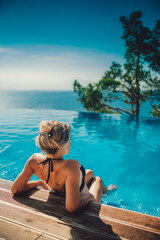 Charming, sexy girl sitting by the pool, which is on the background of the sea