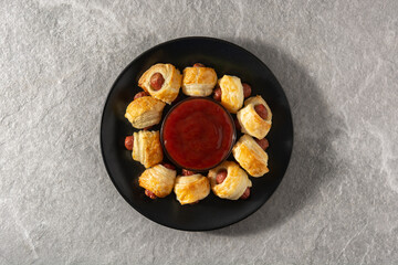 Pigs in blankets. Mini sausages wrapped in puff pastry with ketchup sauce on gray stone	