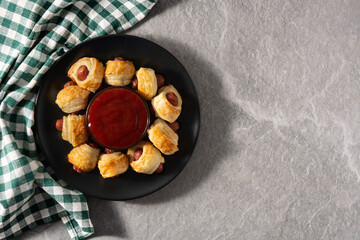 Pigs in blankets. Mini sausages wrapped in puff pastry with ketchup sauce on gray stone	