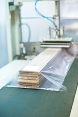 wood flooring planks being covered in plastic protection with factory machine