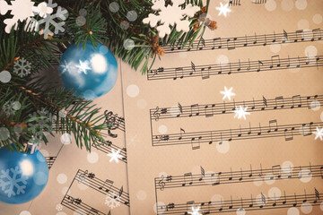 Top view of fir tree branches with Christmas decor on sheet music pages, snowflakes and bokeh effect