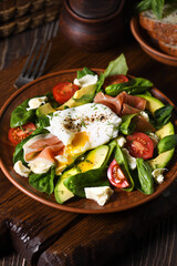 Eggs Benedict (Poached) with Parma ham, slices of avocado, tomato and tender spinach leaves, seasoned with flavored spicy olive oil