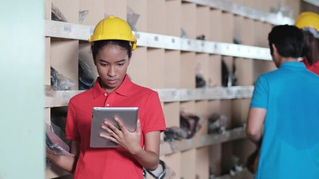 Africa American worker looking at tablets and check the quality of spare parts in the automotive warehouse distribution store.  Engineers wear a safety helmet, vest standing in the factory. 