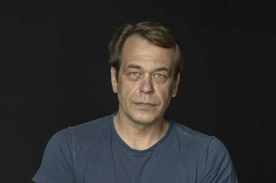 Portrait of a man in a Studio 40-50 years old in a blue t-shirt on a black blurry background, close-up. Maybe he's just a buyer, an actor or a truck driver, a loader or a military pensioner