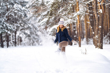 Fototapeta na wymiar Happy winter time. Cute woman playing with snow in snowy forest. Young lady in winter clothes enjoying the winter. Winter holiday.