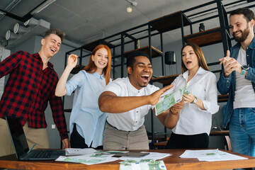 Low-angle shot of cheerful multi-ethnic employees celebrating victory and big profit at office workplace. Cheerful excited young business man and woman throwing away banknote. Rain of money