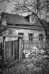 An old village house with a rickety wooden fence. Black and white photo.