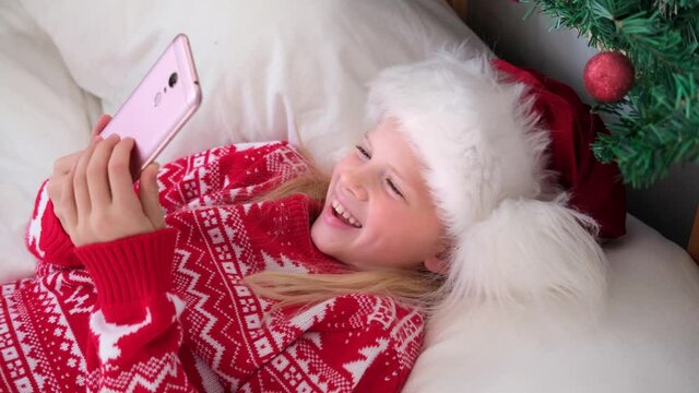 4k Christmas online congratulations. Smiling girl using mobile phone for video call. Child talking friends and parents.