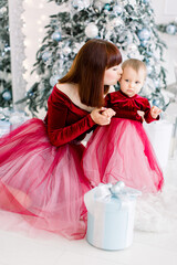 Christmas holidays, family concept. Pretty young mom kissing her little sweet beautiful daughter, spending winter time together, sitting on the floor in front of Christmas tree