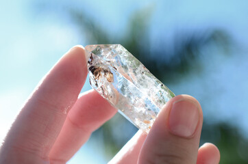 Clear quartz being held in woman's hand. Clear quartz point in the sunlight. Healing quartz with inclusions, intricate details. 