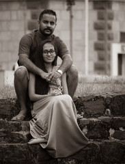 Lovely young married couple sitting down in the stone steps of Galle fort, sepia-tone photograph, celebrating and embracing the pregnancy, expecting the child together.