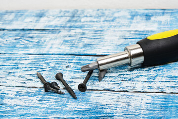 Screwdriver, screws and wooden bars on wooden background