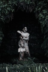 Fototapeta na wymiar Estatua femenina en una fuente de agua rodeada de vegetación con fondo oscuro
