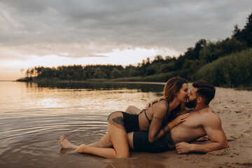 Passionate photo session on the shore in the water. Young couple in the evening by the lake....