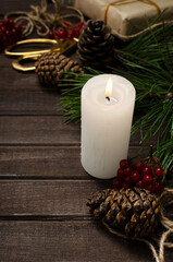 Fototapeta na wymiar Vertical image.White candle, cones, present, green fir branches and red viburnum on the wooden table