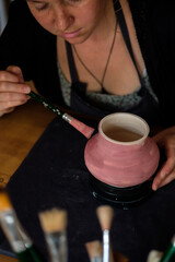 Woman potter paints a handmade vase.