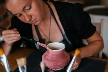 Woman potter paints a handmade vase.