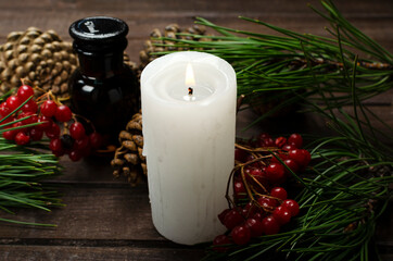 Closeup of white candle, glass bottle, red viburnum, green fir branches on the wooden desk