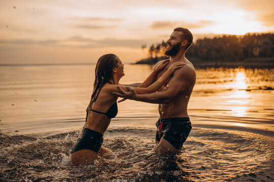 Romantic photo session in the water. A guy and a girl swim in the lake in the evening. Beautiful sunset.