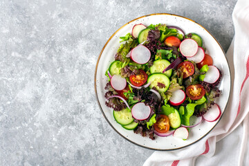 Healthy vegetable salad of cherry tomatoes, cucumber slices, green and purple lettuce leaves, onions and olive oil in plate on concrete table Top view Flat lay Diet, mediterranean menu Vegan food