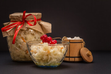 Fermented cabbage with herbs and spices in glass bowl and jar on the black background