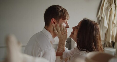 Loving couple enjoying romantic date in pottery workshop. Lovers having fun smearing each other with clay laughing and kissing.