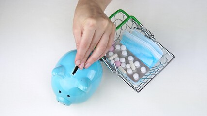 The hand puts the coins in the piggy Bank. A small shopping basket with medicines on a white background.
