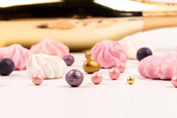golden gift bottle of champagne, multicolored dragee candies and meringue cake on white wooden table