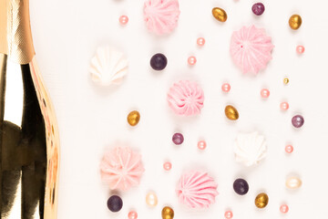 golden gift bottle of champagne, multicolored dragee candies and meringue cake on white wooden table