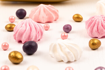 multicolored dragee candies and meringue cake scattered on a white wooden table