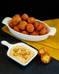 Traditional Middle Eastern food, Falafel (tamiya) with hummus and pickles on black wooden background and yellow table cloth.