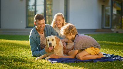 Portrait of Father, Mother, and Son Having Picnic on the Lawn, Posing with Happy Golden Retriever Dog. Idyllic Family Have Fun with Loyal Pedigree Doggy Outdoors in Summer House Backyard.