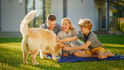 Portrait of Father, Mother and Son Having Picnic on the Lawn, Posing with Happy Golden Retriever Dog. Idyllic Family Has Fun with Loyal Pedigree Puppy Outdoors in Summer House Backyard.