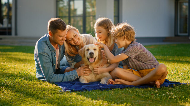 Smiling Portrait of Beautiful Family of Four Having Picnic on the Lawn, Posing with Happy Golden Retriever Dog. Idyllic Family Have Fun with Loyal Pedigree Dog Outdoors in Summer House Backyard.
